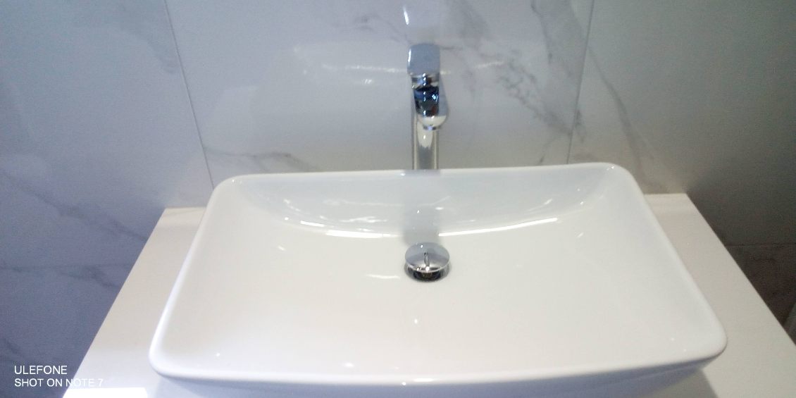 White vessel sink with tall chrome faucet against marble-look tile